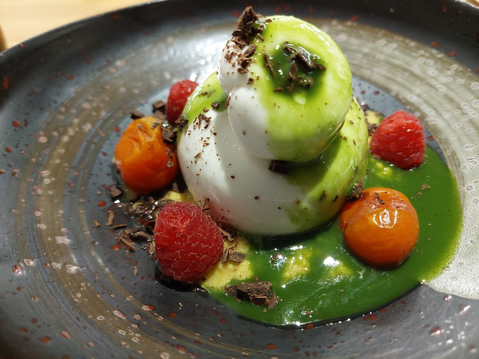 Postre emplatado con frutos rojos y coulis verde sobre plato de piedra