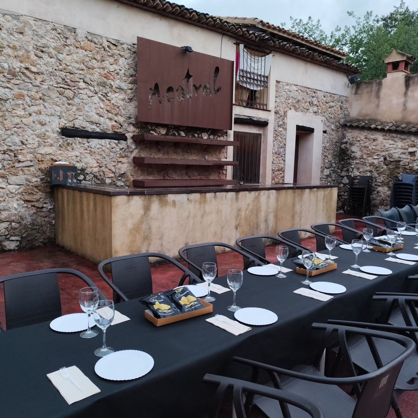 Mesa larga vestida de negro en un patio de piedra, preparada para una comida privada