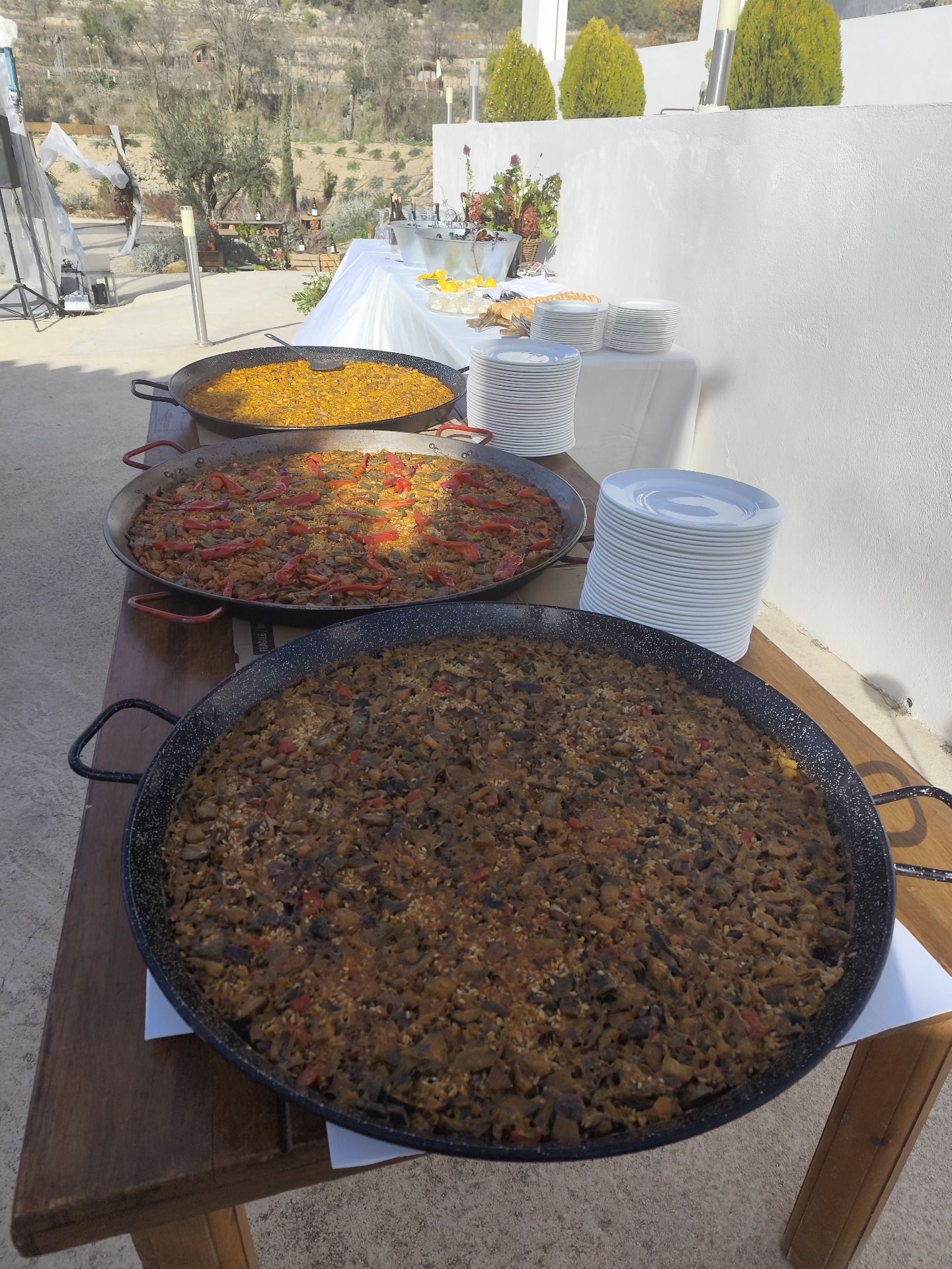 Tres paellas de arroz servidas en una mesa exterior junto a la vajilla